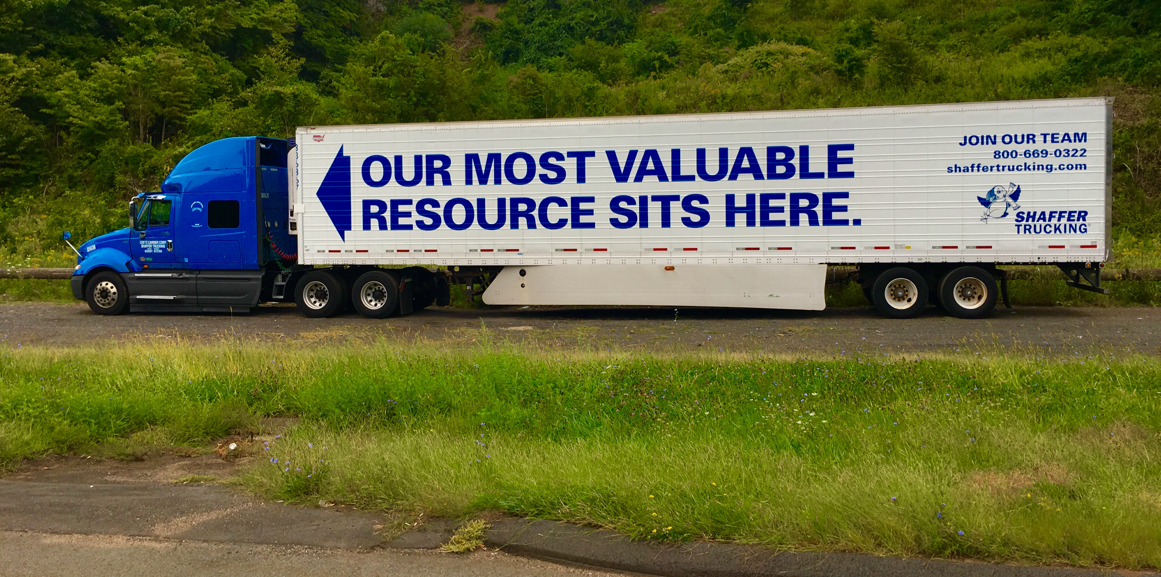 Older truck driver standing beside semi-tractor reviewing paperwork on clipboard