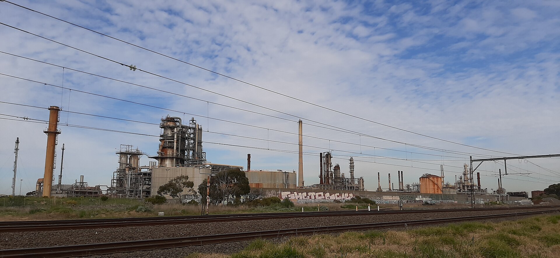 Oil barrels stacked at refinery with price chart showing decline
