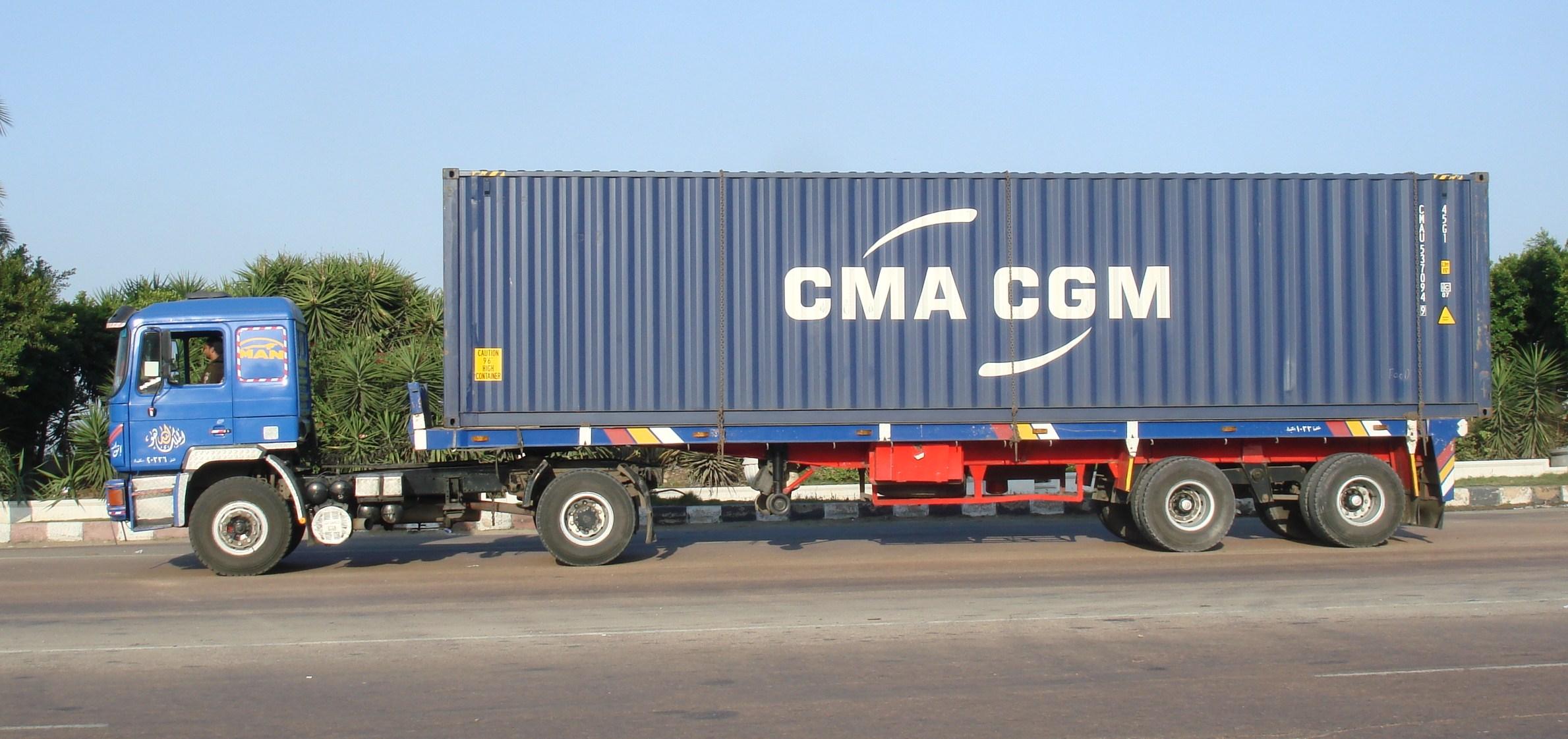 Container ship at port terminal with stacked shipping containers and truck chassis in foreground