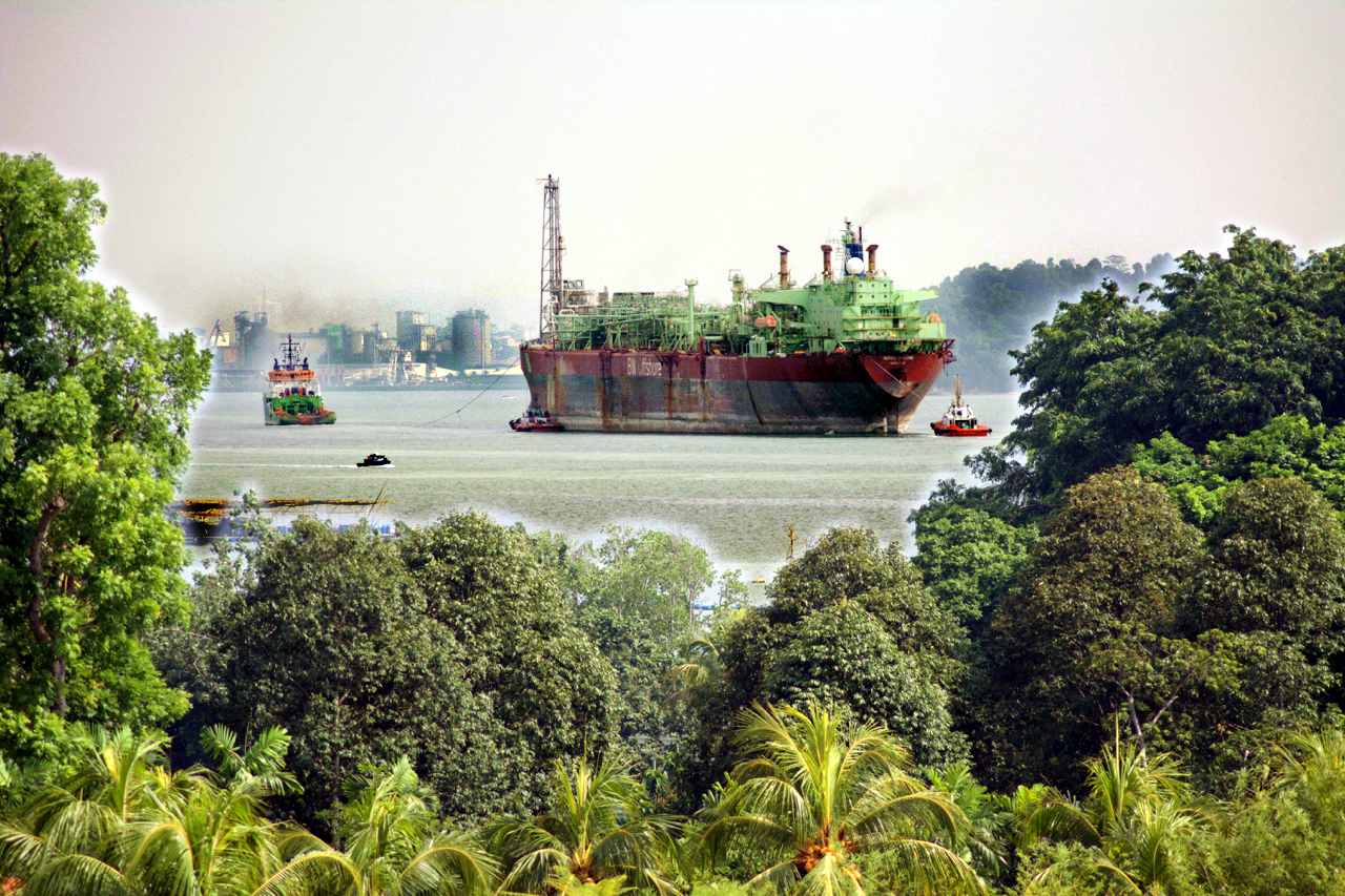Oil barrels stacked at a refinery terminal with price charts showing upward trend