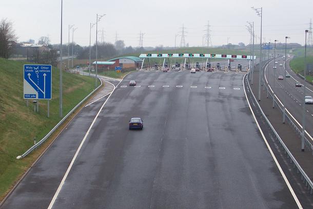 Commercial truck approaching toll plaza with electronic and cash lane options on multi-lane highway